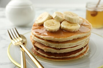 Delicious pancakes with bananas and honey on white table, closeup