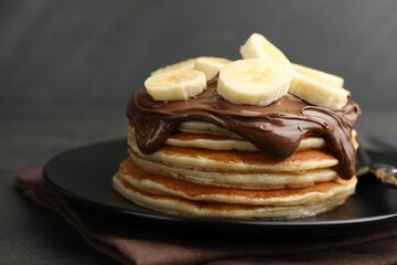 Tasty pancakes with chocolate spread and sliced banana on table against gray background, closeup