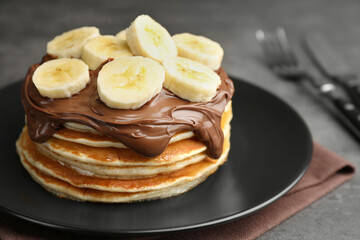 Tasty pancakes with chocolate spread and sliced banana on table, closeup