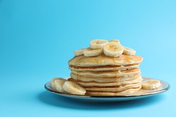 Tasty pancakes with sliced banana and honey on light blue background, space for text