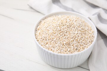 Dry barley groats in bowl on white wooden table, closeup. Space for text