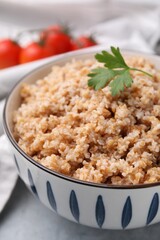 Tasty wheat porridge with parsley in bowl on grey table, closeup