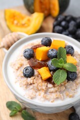 Tasty wheat porridge with pumpkin, dates and blueberries in bowl on table, closeup