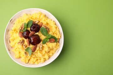 Tasty cornmeal with dates, nuts and mint in bowl on green table, top view. Space for text