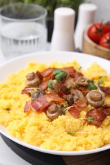 Tasty cornmeal with bacon, mushrooms and microgreens in bowl on table, closeup