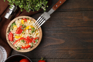 Cooked bulgur with vegetables in bowl on wooden table, flat lay. Space for text