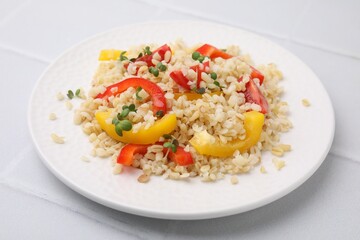 Plate of cooked bulgur with vegetables on white tiled table