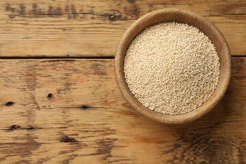 Dry quinoa seeds in bowl on wooden table, top view. Space for text