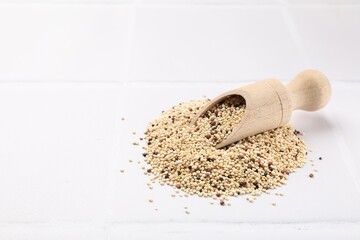 Scoop with raw quinoa seeds on white tiled table. Space for text