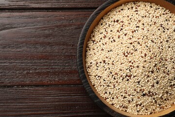 Raw quinoa seeds in bowl on wooden table, top view. Space for text