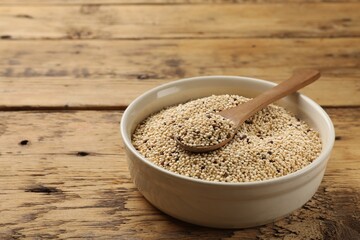 Raw quinoa seeds and spoon in bowl on wooden table, closeup. Space for text