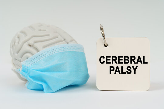 On a white surface there is a brain with a blue mask and a notepad with the inscription - CEREBRAL PALSY