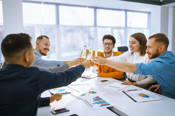 Business people celebrate with glasses of champagne in the office at a corporate event. A group of young people are having fun in the office. Holidays, business concept.