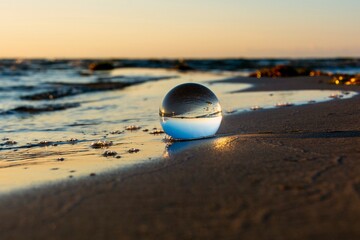 Fototapeta na wymiar Beach and sea reflected in a sphere lying in the sand in the waves