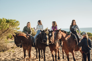 Group of female friends drinking from plastic cups while riding horses