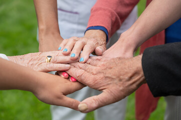 Concept of family, aging society or teamwork, hands showing unity with putting hands together, senior wrinkled hands of old people together with other young people hands. High quality photo