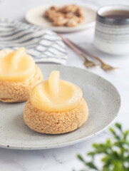 A French cream puff crack bun (Choux au Craquelin) topped with poached pear fruit with cup of tea,  plate and spoon in background. It's a dessert base of savory choux dough, pastry cream.