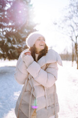 Obraz premium Winter portrait of a happy woman in a snowy park. Young woman in warm clothes having fun with snow outdoors. Fun, weekend concept