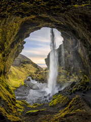 Wasserfall auf Island von hinten mit Felsbogen und grünem Moos.