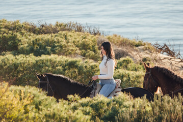 Smiling female horseback rider riding horse near sea