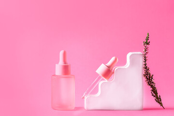Set of skin care serums in pink bottles with dropper on bright pink background with flowers and decorations. Natural organic cosmetic products.