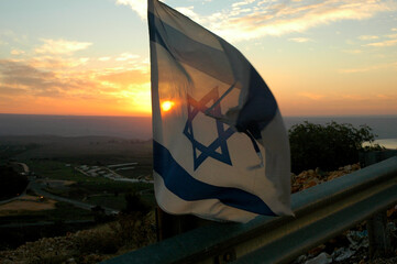 An Israeli flag tied to a guard rail at sunrise