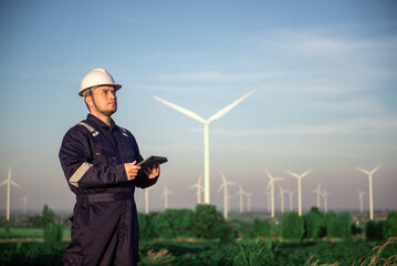 A wind turbine maintenance engineer is standing and inspecting the operation of wind turbine blades and inspecting various systems