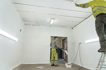 Two Skilled Workers in Overalls Transform a Spacious Room or Garage with Paint.