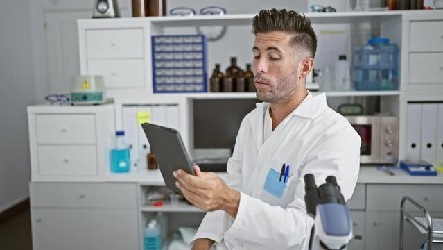 Young, attractive hispanic man, scientist, engaging in a crucial online video call conference at the lab, armed with a touchpad amidst science research.