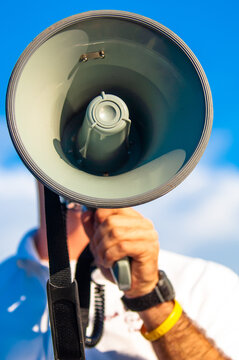 closeup of a man speaking into a megaphone against a blue sky