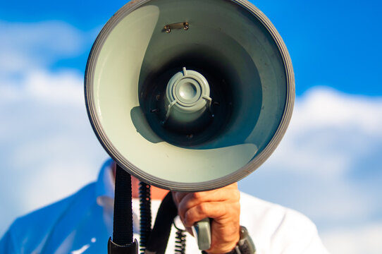 closeup of a man speaking into a megaphone against a blue sky