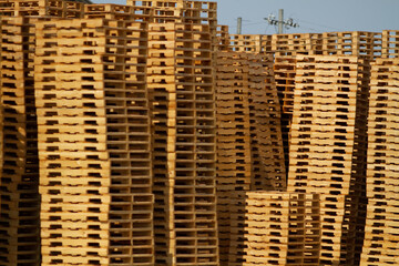 multiple wooden columns of shipping pallets piled high in an outdoor yard of a lumber mill where they are manufactured from raw materials and sold to shipping logistics carriers to transport goods