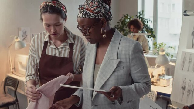 Zoom-out shot of female African American atelier owner organising manufacturing process of new apparel collection while guiding sewing workshop personnel