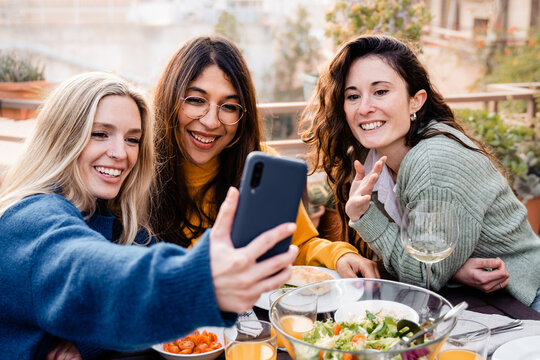 Happy friends having fun at vegan dinner party. Group of people taking selfie picture while eating outside patio restaurant.