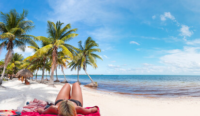 Blonde Girl in black swimwear and sunbathes on the beach Palm tree in the background - Cancun,...