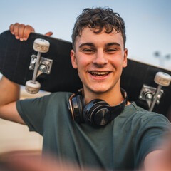 One man young adult caucasian teenager stand outdoor with skateboard on his shoulder and headphones posing at basketball court portrait happy confident wear shirt casual real person copy space © Miljan Živković