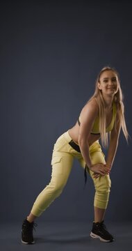Beautiful blond girl in black outfit dancing zumba against dark blue background. Vertical video.