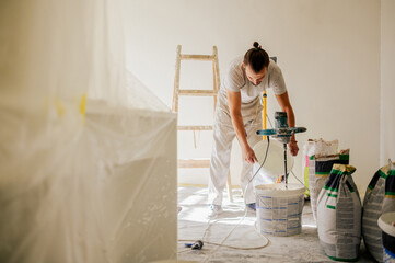 A laborer is adding water to a plaster mixture while renovating home.