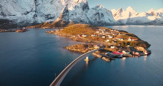Aerial view of snowy rocks, islands with rorbuer, sea bay, bridge, mountains, road, blue sky at sunrise in winter. Beautiful top drone view of Hamnoy and Reine village, Lofoten islands, Norway. Nature