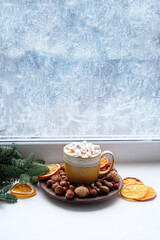 cocoa mug with marshmallows, dried orange slices, nuts, fir branches on windowsill. New year and Christmas holidays background. festive winter season. home hygge comfort in cold weather