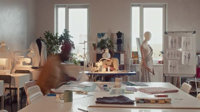 Time lapse of diverse workers working in atelier studio sewing on garment machines, drawing sketches and creating new clothing collection