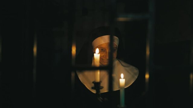 Possessed nun holding burning candles and walking in haunted monastery chambers