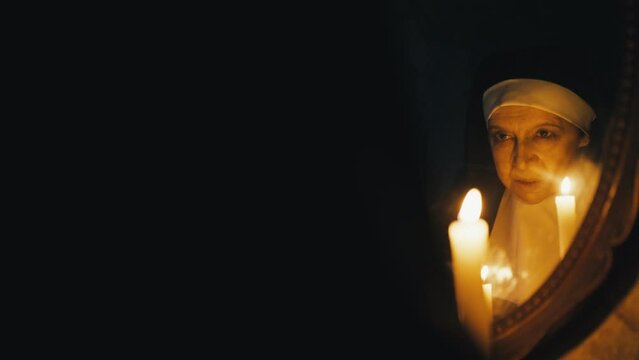 Possessed nun holding burning candles and casting spells in front of mirror