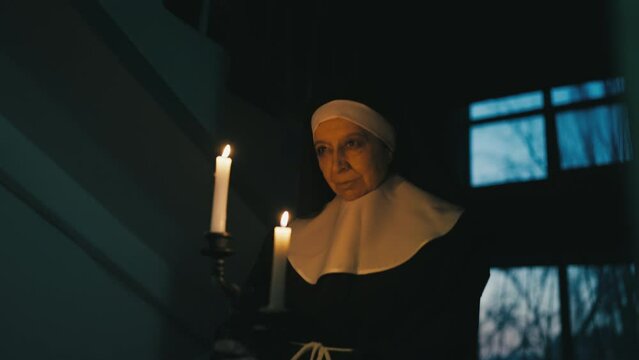 Evil nun ghost holding burning candles and walking in haunted building at night