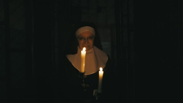 Evil nun walking with burning candles in chambers of haunted monastery, horror