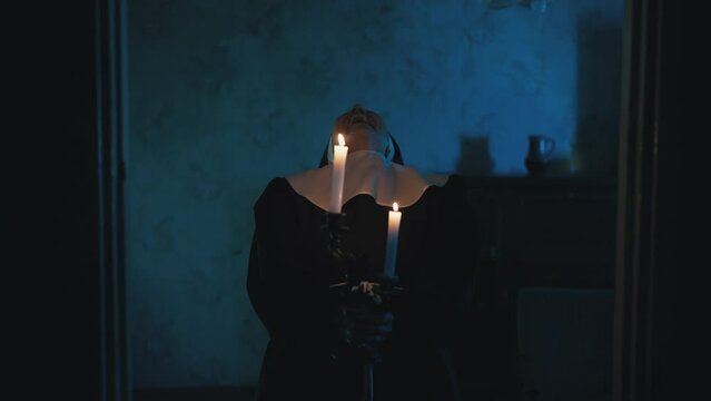 Portrait of evil nun holding burning candles, tilting her head back and laughing