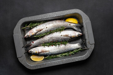 Raw grey mullet fish with spices and herbs in the cooking pan on black stone table top view. Raw fish ready to cook.