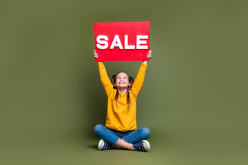 Full size photo of nice schoolgirl with tails wear yellow pullover look at sale board over head isolated on khaki color background