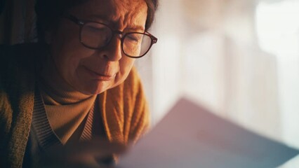 Lonely sad grandmother reading a letter with bad news and crying, financial debt