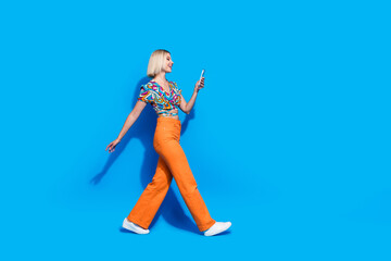 Fototapeta na wymiar Full length profile portrait of gorgeous positive person walk use smart phone empty space isolated on blue color background